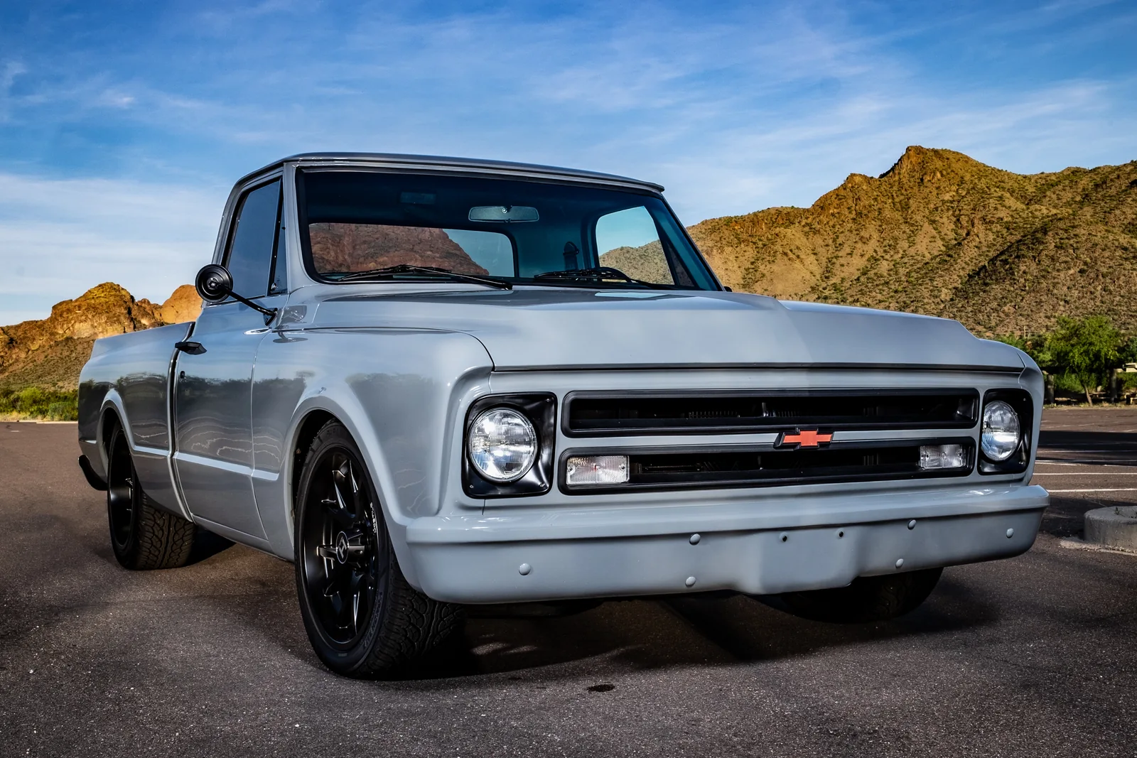 A silver classic Chevrolet pickup with desert mountains behind it