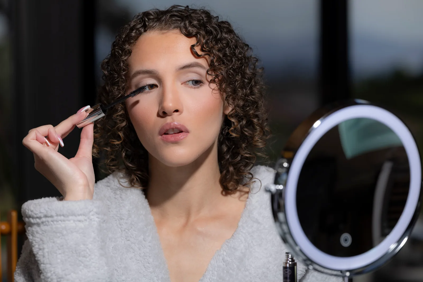 A woman applying lash treatment while looking into a small round mirror