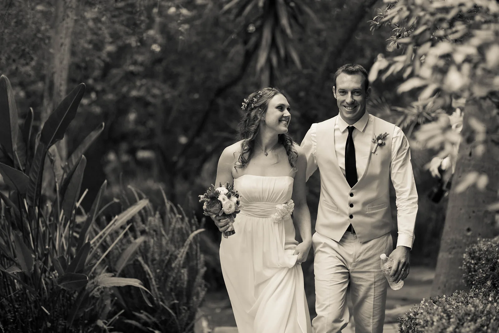 A bride and groom walking through a garden, photographed in black and white